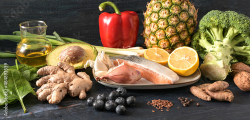 Healthy vegetables, fish, fruits, nuts and spices, food for an anti-inflammatory and antioxidant diet on dark rustic wood, panoramic format, selected focus, narrow depth of field photo