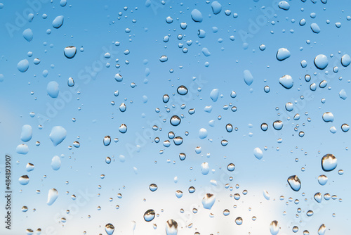 Raining droplets on glass window circle different shapes closeup selective focusing. Blue white cloud sky background. Beautiful freshness nature scenery.