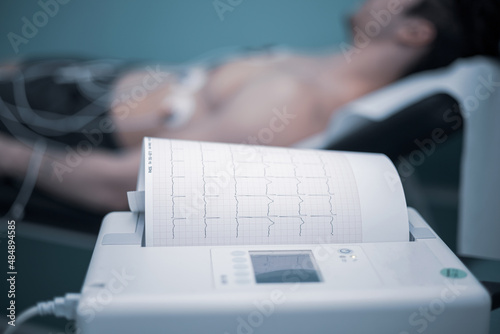 doctor with electrocardiogram equipment doing cardiogram test to male patient in hospital clinic
