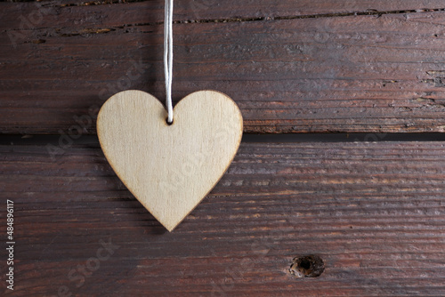 Natural heart shape pendant on a dark rustic wood wall, symbol of love in everyday life and holidays like valentines, mother's day, father's day and birthday, copy space