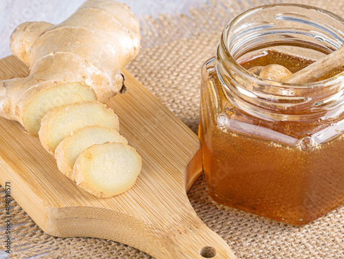 Honey in a glass jar with a spoon for honey. Fresh sliced ginger on a light wooden background. Top view, Close-up