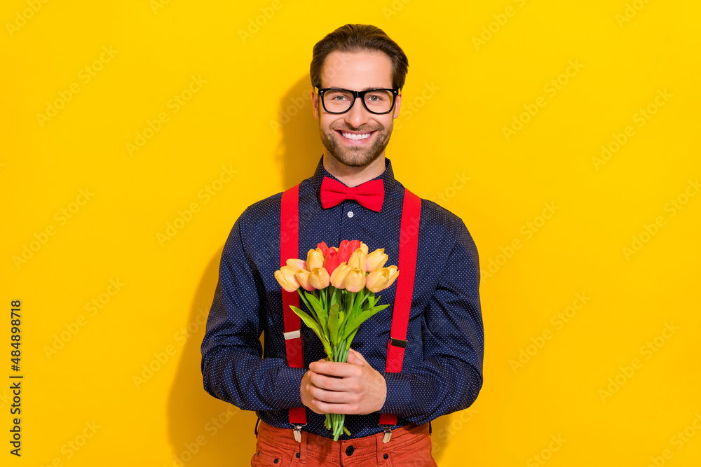 Photo of young cheerful guy hold bunch of tulips present anniversary event isolated over yellow color background Photo of young cheerful guy hold bunch of tulips present anniversary event isolated over yellow color background