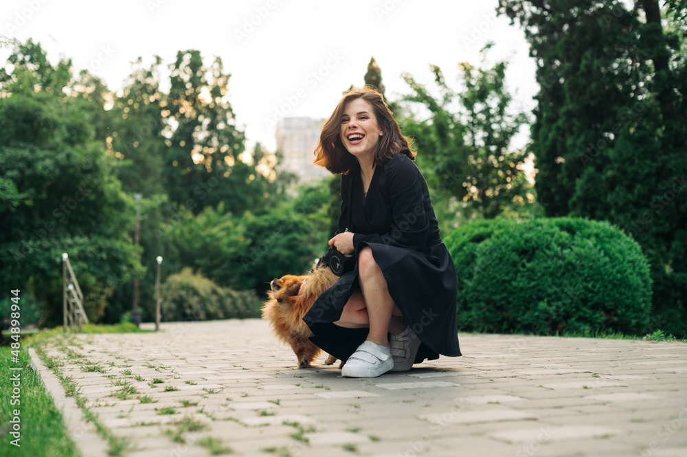Positive woman with a dog on a walk sitting on the pavement with a smile on his face on a background of the park.