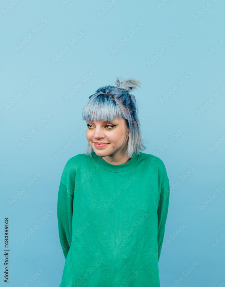 © bodnarphoto - Cheerful teen girl with blue hair and in a green sweatshirt looks aside with a smile, isola on a blue background.vertical