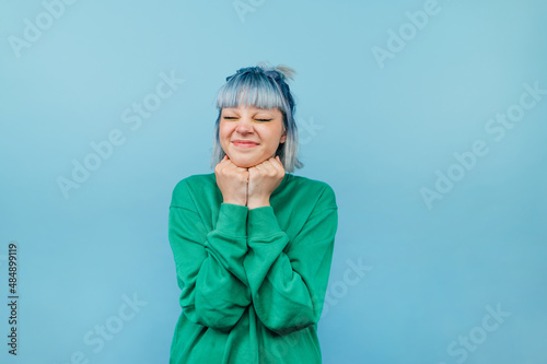 Portrait of joyful girl with colored hair on a blue background with a smile on his face and eyes closed happy.