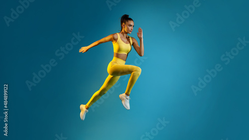 Motivated Young Lady Jumping Posing In Mid-Air Over Blue Background