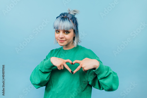Beautiful teen girl in a green sweatshirt and colored waltz shows a heart gesture and looks at the camera with a smile on his face.