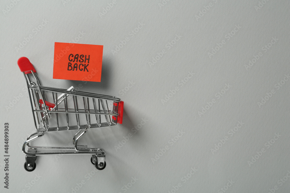Card with word Cashback and shopping cart on light grey background, flat lay. Space for text