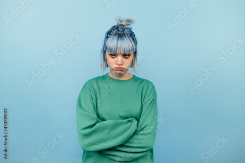 Foto Portrait of a displeased teen girl with long hair standing on a blue background and looking away
