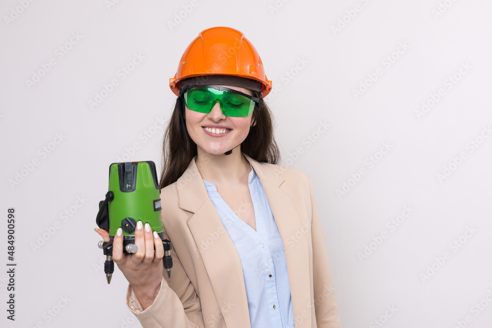 A girl in an orange helmet and a laser level in her hands on a white background.