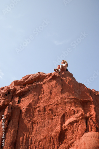 Low level shot of caucasian woman sitting in a rock with clear sky.