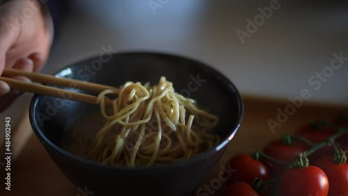 Closeup of woman girl eating the Chinese dish of noodles with tomatoes in a black bowl with chopsticks at a restaurant or at home.