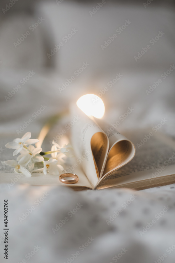 Golden ring and open book with folded sheets in heart shape in bed. Wedding concept, Happy Valentine's Day