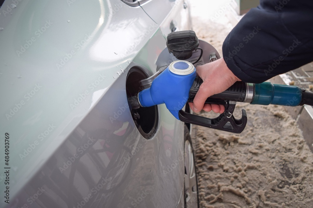 A man's hand directs a hose into the gas tank of a car at a gas station on a winter day A man's hand directs a hose into the gas tank of a car at a gas station on a winter day