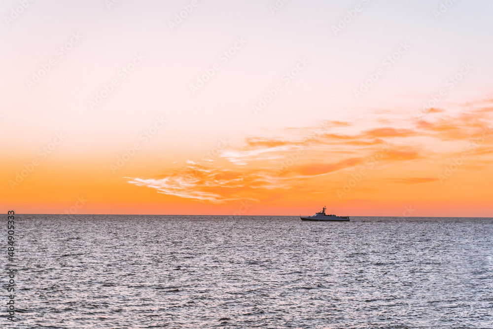 Silhouette of a ship at sea with an orange sunset sun, horizon line between sky and water
