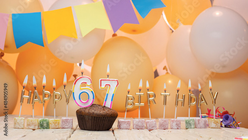 Happy birthday greetings for the year 67 from golden letters of candles burning against the background of mine space balloons. Beautiful birthday card with a muffin for sixty-seven years. photo