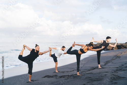 Men and woman in sportive wear doing yoga exercises for healthy vitality and wellness, youngmale and female yogi warming up and stretching body muscles before morning training at coastline