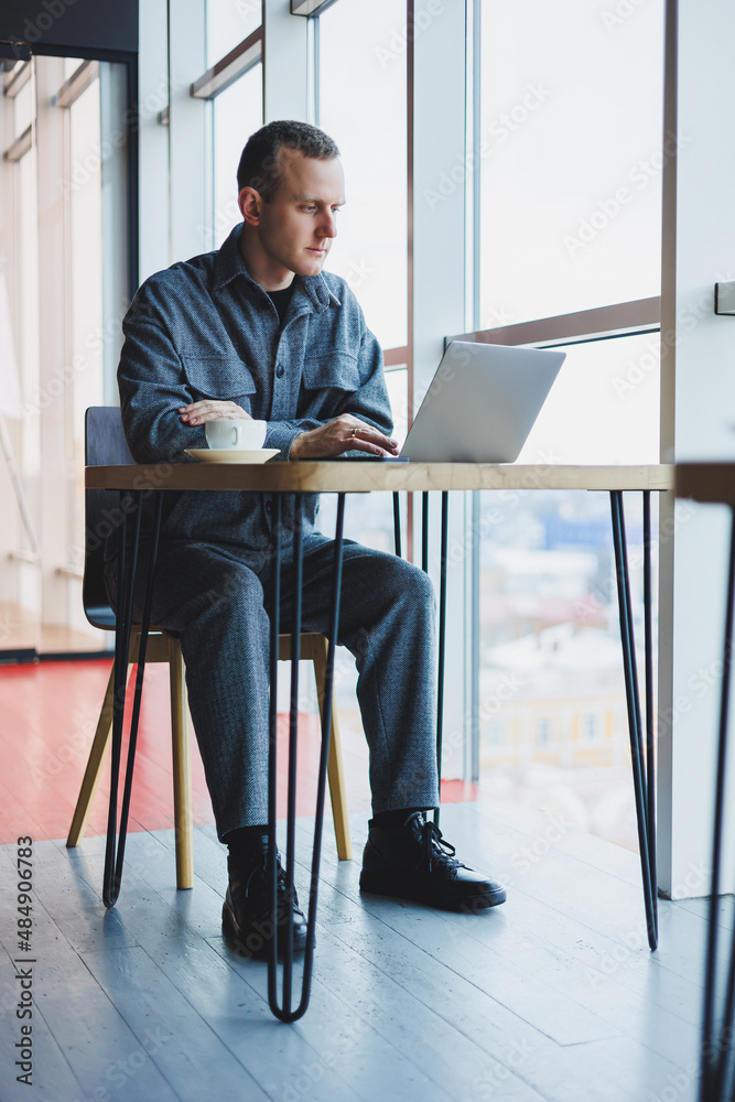 A young successful businessman in a suit drinks coffee and works in a cafe on wireless free internet on a laptop, sitting alone at a table in a cafe. A young successful businessman in a suit drinks coffee and works in a cafe on wireless free internet on a laptop, sitting alone at a table in a cafe.