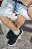 Legs of boy wearing denim shorts sitting on armchair and holding smartphone near brother in waiting room of airport extreme closeup