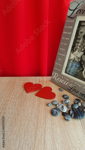 Symbol for valentine's day. two wooden hearts, gray pebbles, a gray photo frame with a "love" inscription on a background of draped red fabric