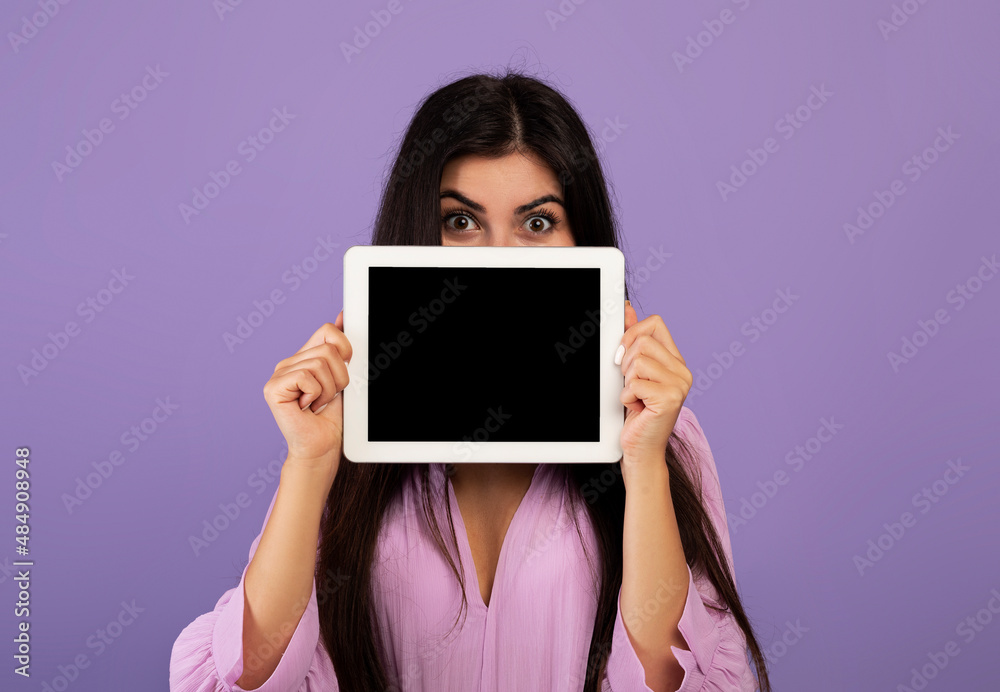 Pretty armenian woman hiding her face behind tablet with blank screen, showing nice dating mobile application on pad Pretty armenian woman hiding her face behind tablet with blank screen, showing nice dating mobile application on pad