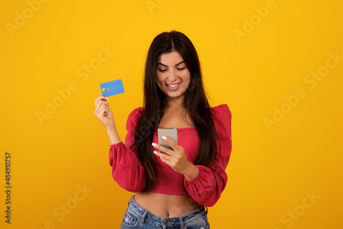 Mobile banking concept. Excited armenian woman holding smartphone and credit card, using application for e-commerce