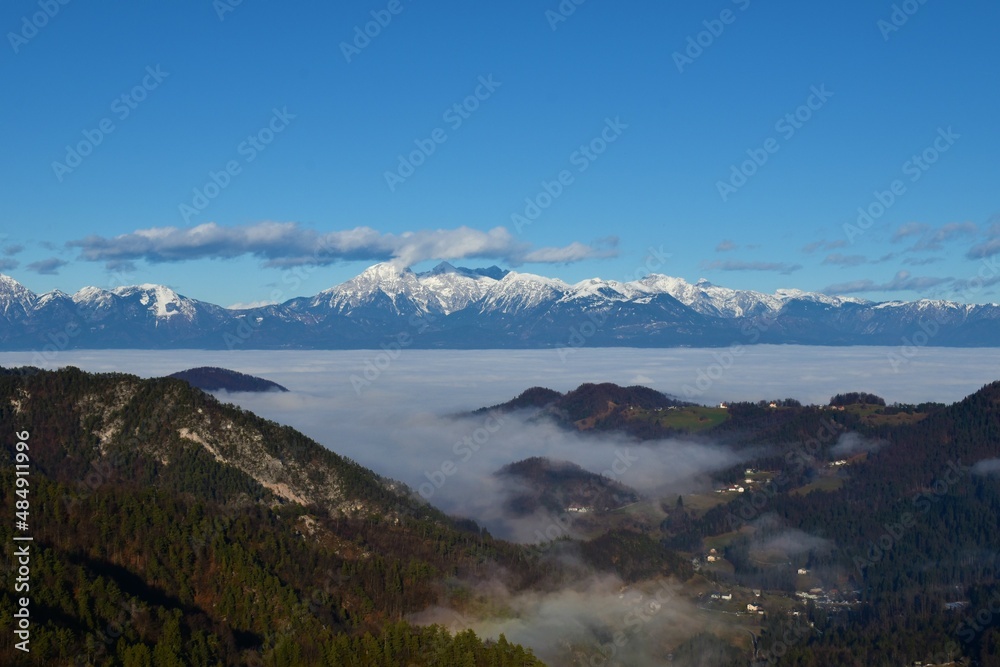 Fototapeta premium View of mountains Grintovec, Skuta and Kocna in Kamnik-Savinja alps in Slovenia with fog bellow the mountains and between the forest covered hills
