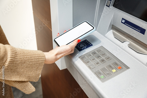 Female hand with mobile phone withdrawing money from atm using NFC contactless wi-fi pay pass system. photo
