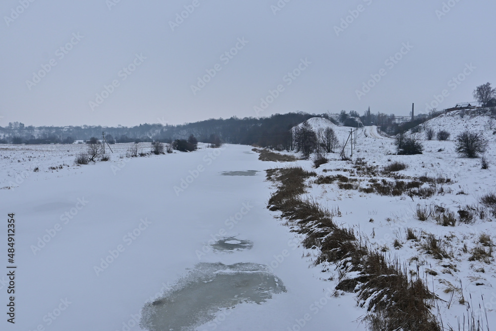frozen river in winter. winter landscape. bank of a mountain river. the river flows through the village. river and forest in winter.