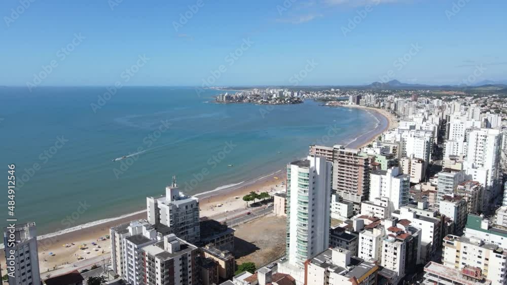 Imagem de drone da Praia do Morro em Guarapari num dia ensolarado com muitas pessoas se divertindo, aproveitando o dia na praia e praticando esportes.	