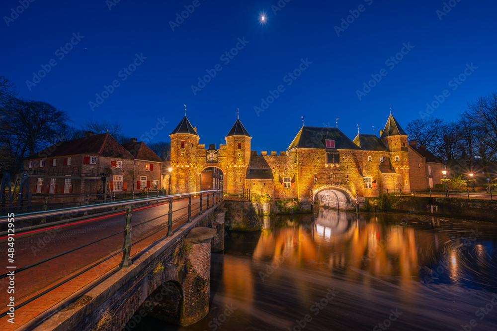 An old medieval gate called the Koppelpoort in Amersfoort with a beautiful reflection and traffic lights during the blue hour