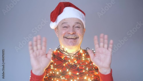 Senior bald man in christmas hat and garland waving hand welcoming friends.