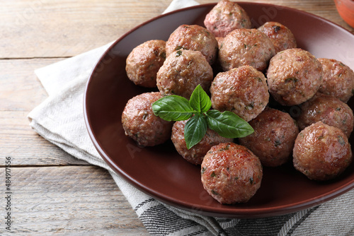 Tasty cooked meatballs with basil served on wooden table