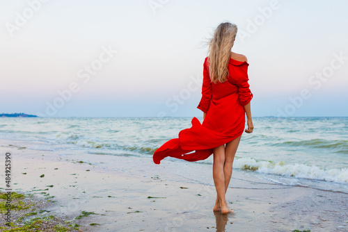 beautiful free woman in red dress in wind on sea beach