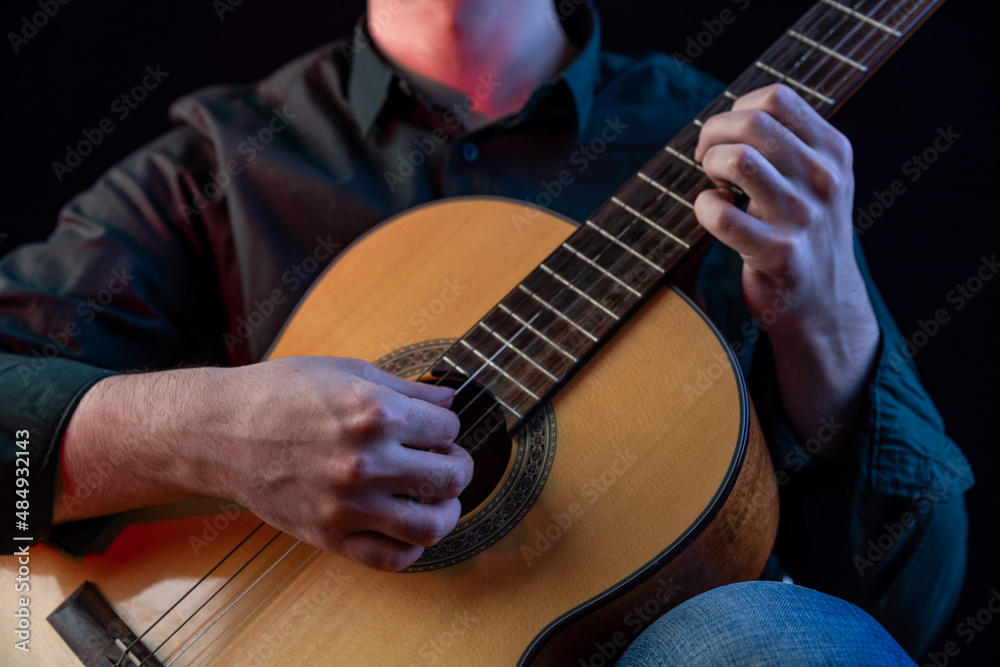 Fototapeta premium The guy in the dark shirt is plucking the strings of a six-string guitar
