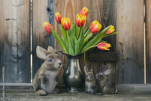 red yellow tulips bouquet in a flower vase and easter rabbits with rustic wood in the background
