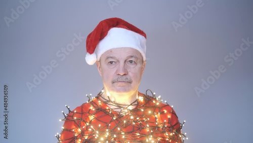 Senior sad man in red christmas hat wrapped in garland.