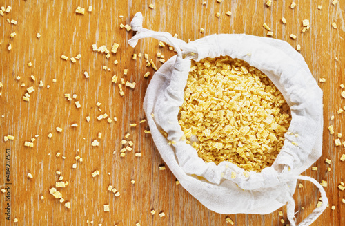  Small flat squares  egg pasta called grattini in white bag on wooden background,yellow  pasta with rough surface  photo