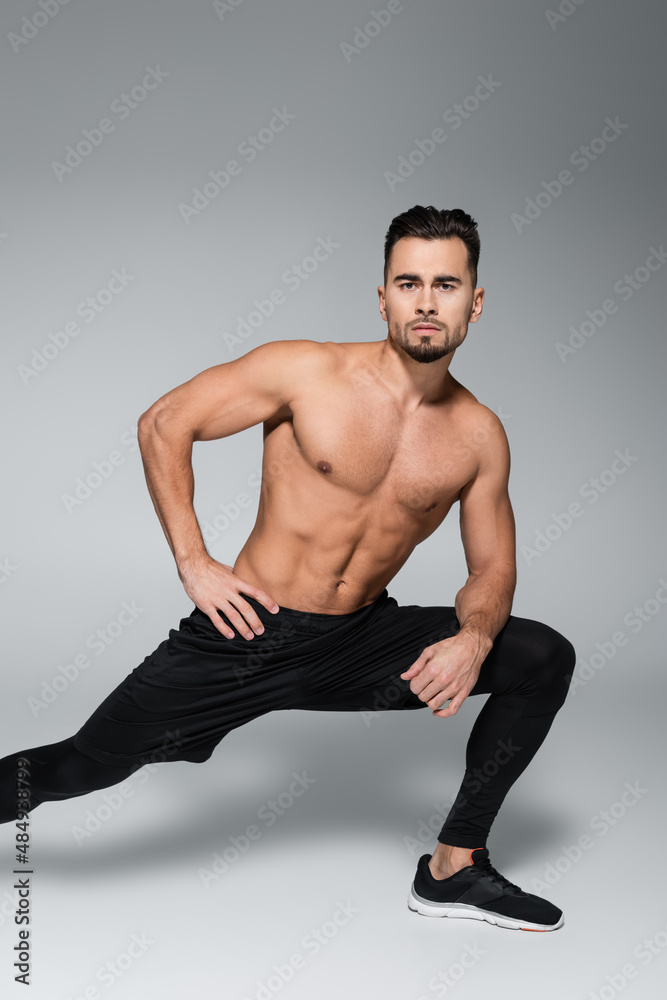 young bearded and muscular sportsman stretching on grey.