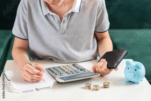 Kid teen boy counting money and taking notes, saving money in a piggy bank. Learning financial responsibility and projecting savings. Concept of finance, business, investment. Lessons in mindfulness