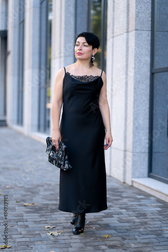 Elegant woman in a stylish black dress posing on a city street