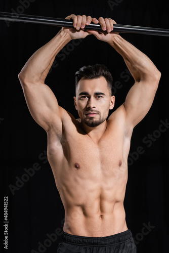 shirtless and muscular sportsman looking at camera near horizontal bar isolated on black. © LIGHTFIELD STUDIOS