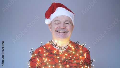 Senior man in red christmas hat wrapped in garland.