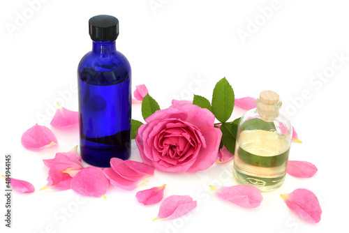 Rose water in blue glass bottle with flower and rose petals on white. Can maintain the skins ph balance, helps to reduce redness of skin, can help heal acne, dermatitis, eczema and is anti bacterial.