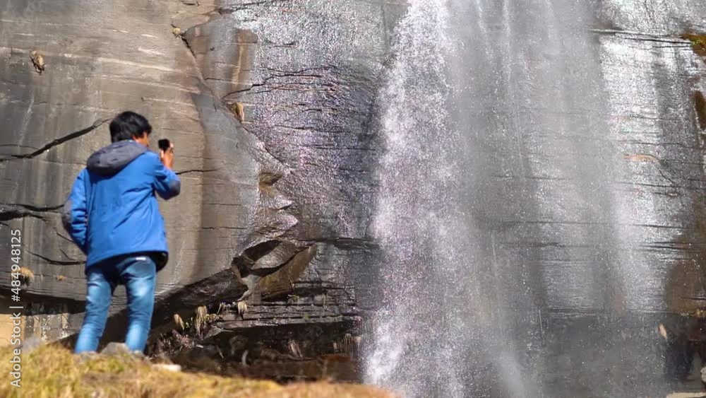 Slow motion shot of the Jogini waterfall with an out of focus photographer taking video of the waterfall while standing in front of it at Manali in Himachal Pradesh, India. Slow motion shot of the Jogini waterfall with an out of focus photographer taking video of the waterfall while standing in front of it at Manali in Himachal Pradesh, India.