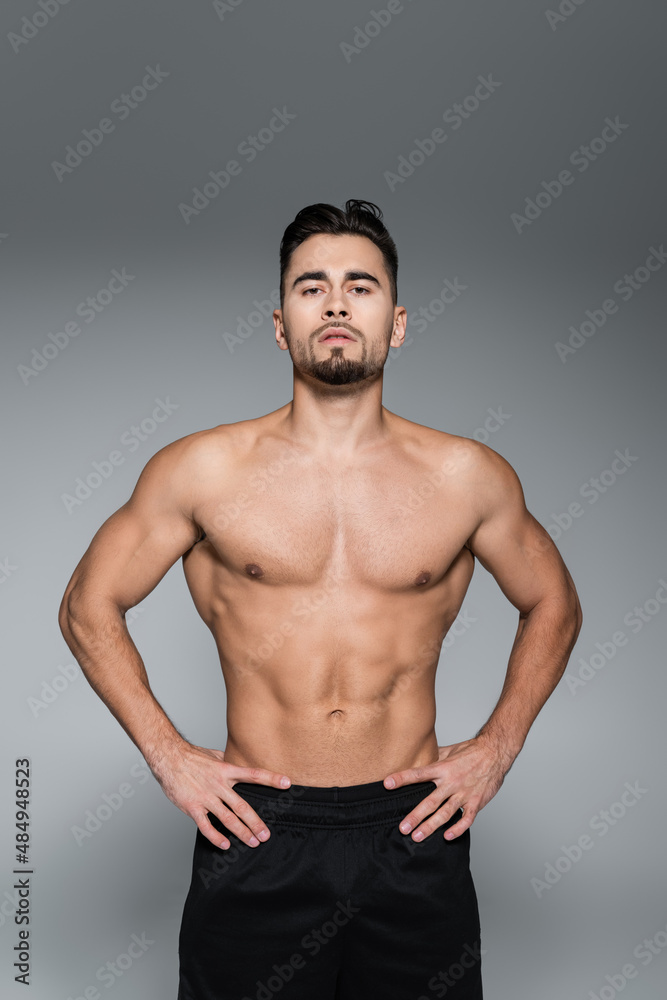 muscular sportsman standing with hands on hips isolated on grey.