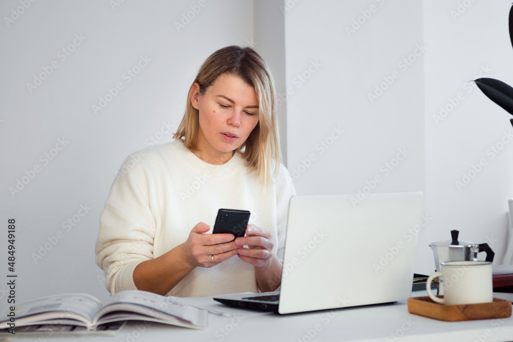 female freelancer online working at table using smartphone, young woman using laptop for business communication or video chatting female freelancer online working at table using smartphone, young woman using laptop for business communication or video chatting