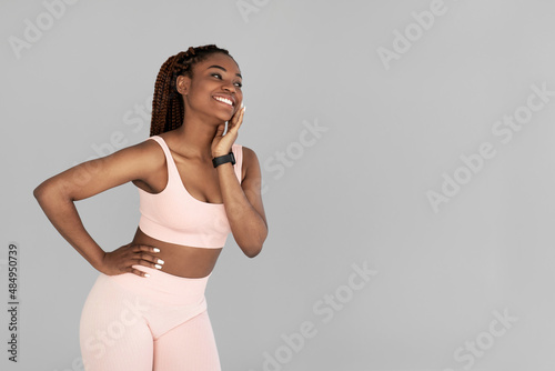 Young black woman in sports outfit wearing fitness tracker, posing and looking aside at empty space on grey background