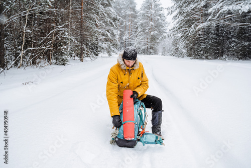 Smiling and happy traveler drinks hot tea or coffee from thermos.Snowy forest and rocks. Climbing the mountain in winter. Survival in the wild.