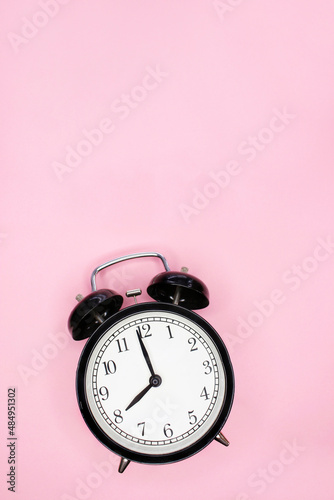 black vinatge alarm clock show 8 o'clock on pink background. copy space